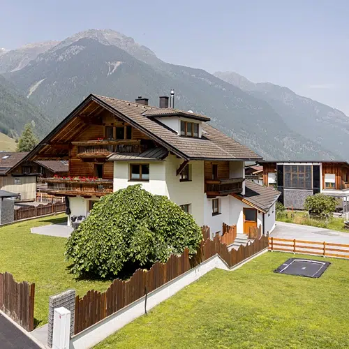 A chalet-style Holiday home apartment Umhausen with fenced yard, mountains, and green lawn.
