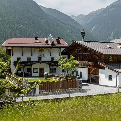Charming alpine holiday home Umhausen with wooden details, set against green hills and mountains.